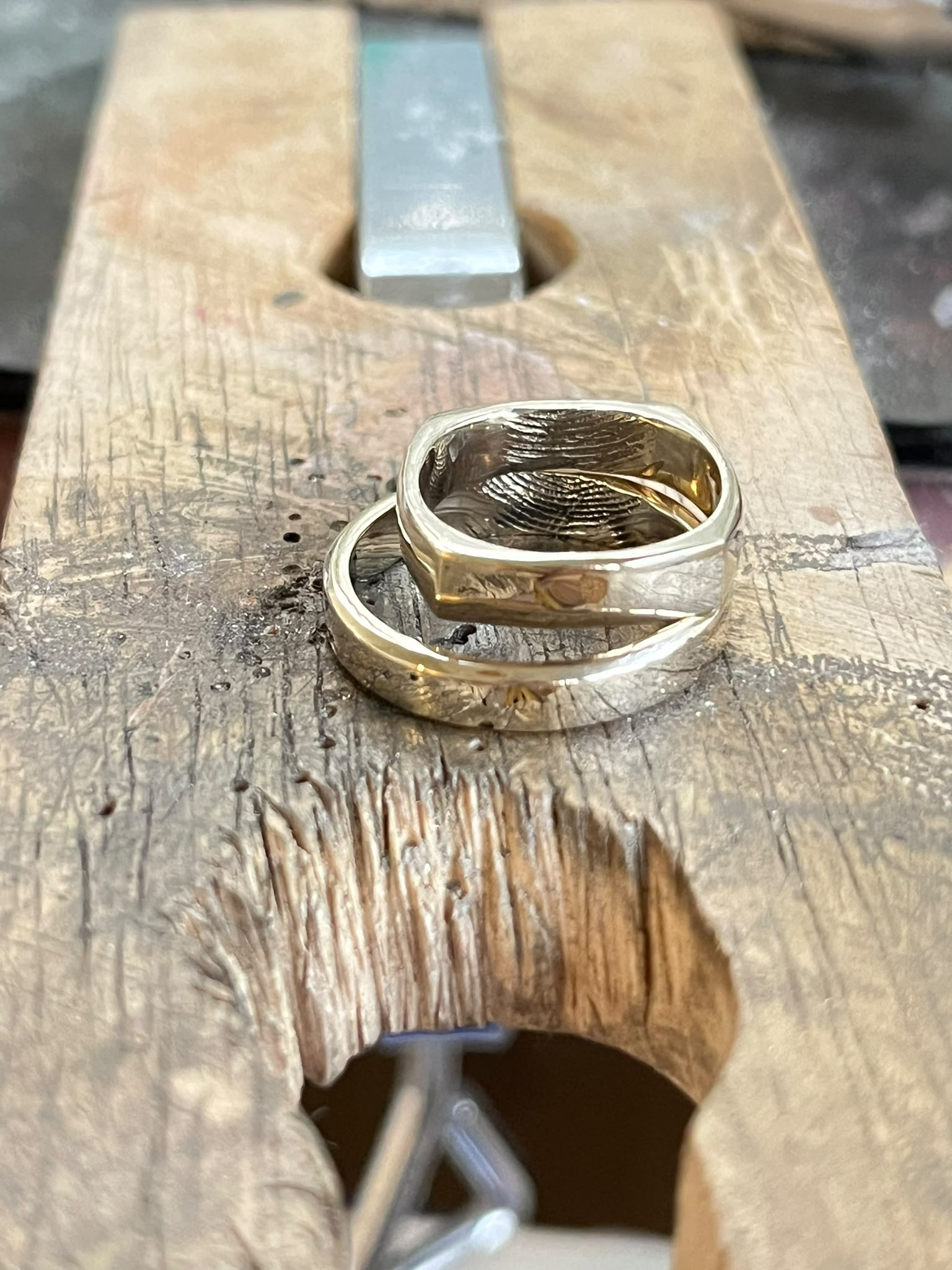 Two gold rings with  a fingerprint-like pattern on the inner band, resting on a wooden workbench.
