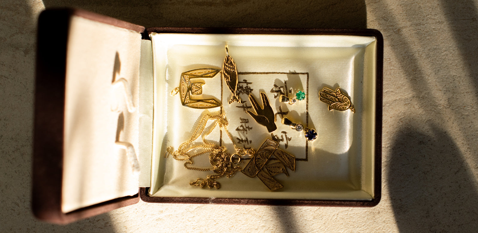 An open vintage jewelry box filled with gold pendents, some featuring colourfull gemstones.