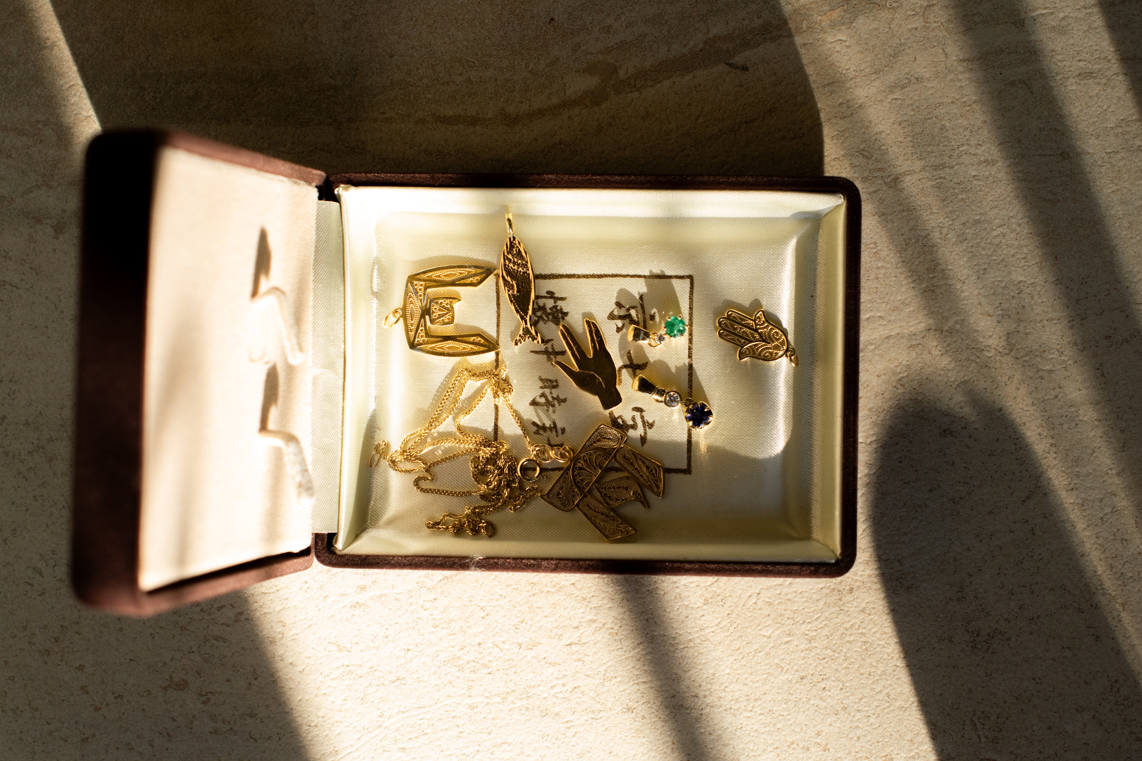 An open vintage jewelry box filled with gold pendents, some featuring colourfull gemstones.