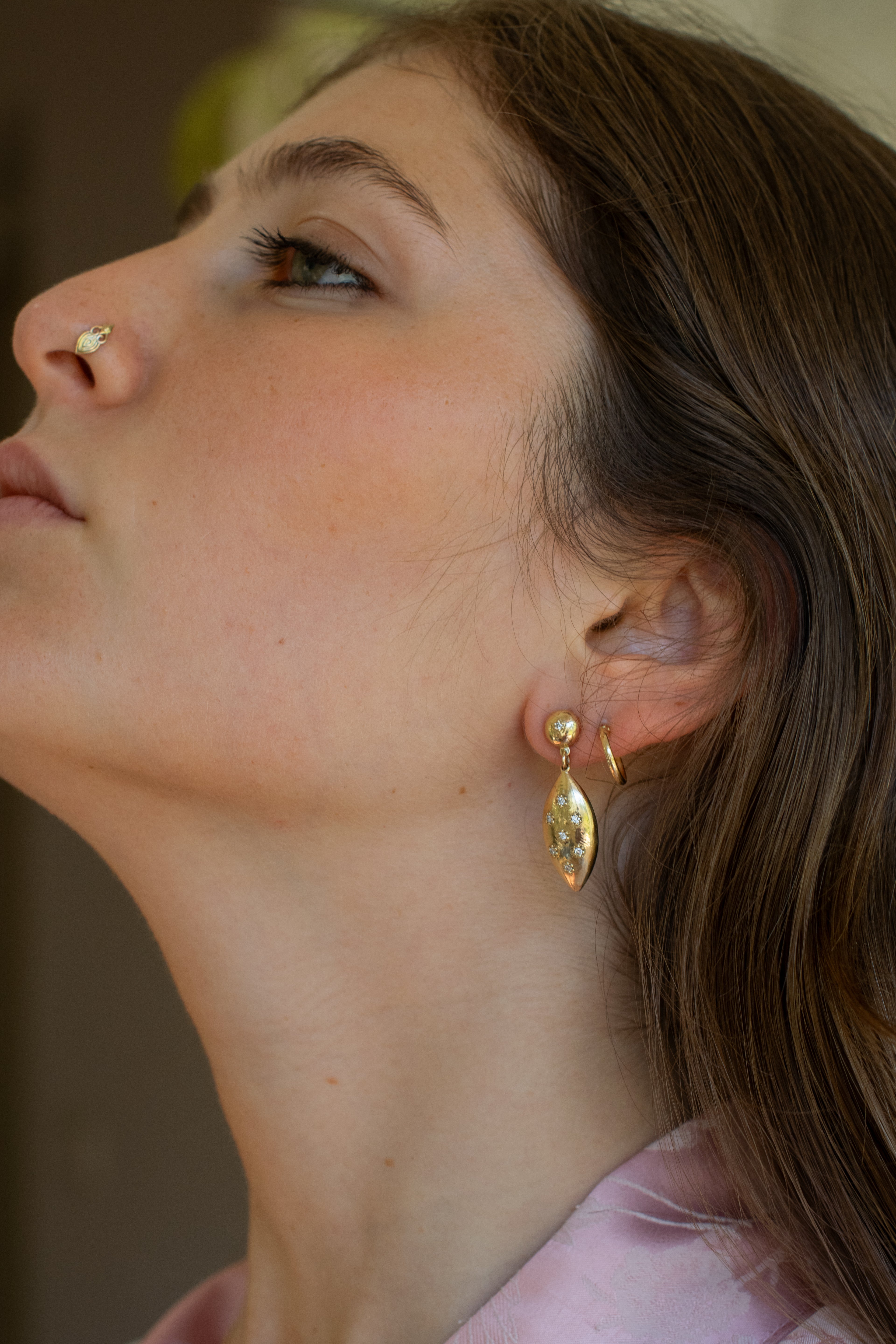 A  side profile of a woman wearing a gold teardrop-shaped dangle earring , along with a gold nose ring.