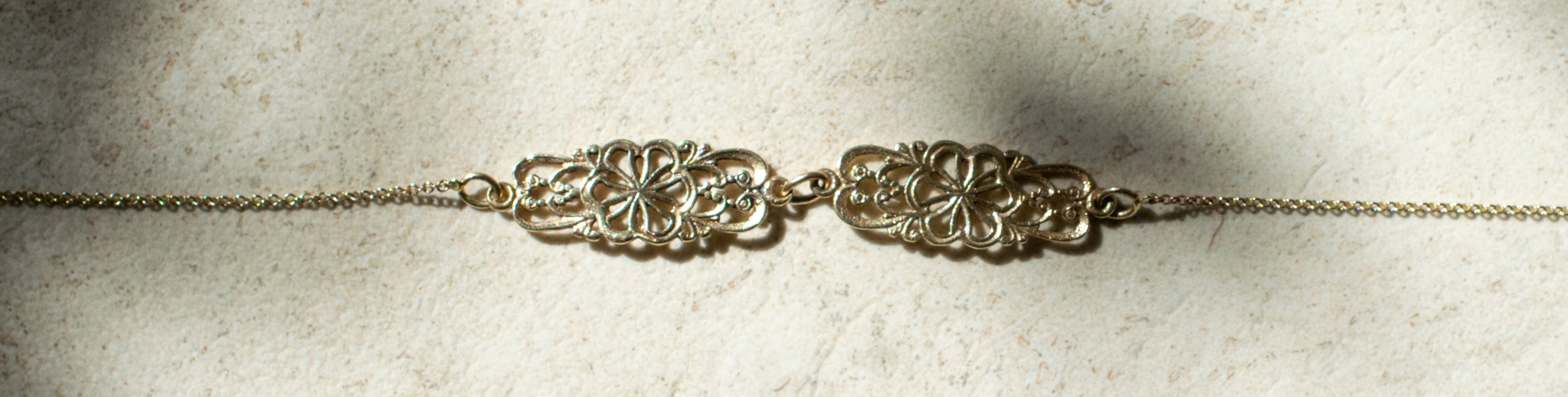 A delicate gold chain neckiace featuring two  interlocking floral or scrollwork links in the center.