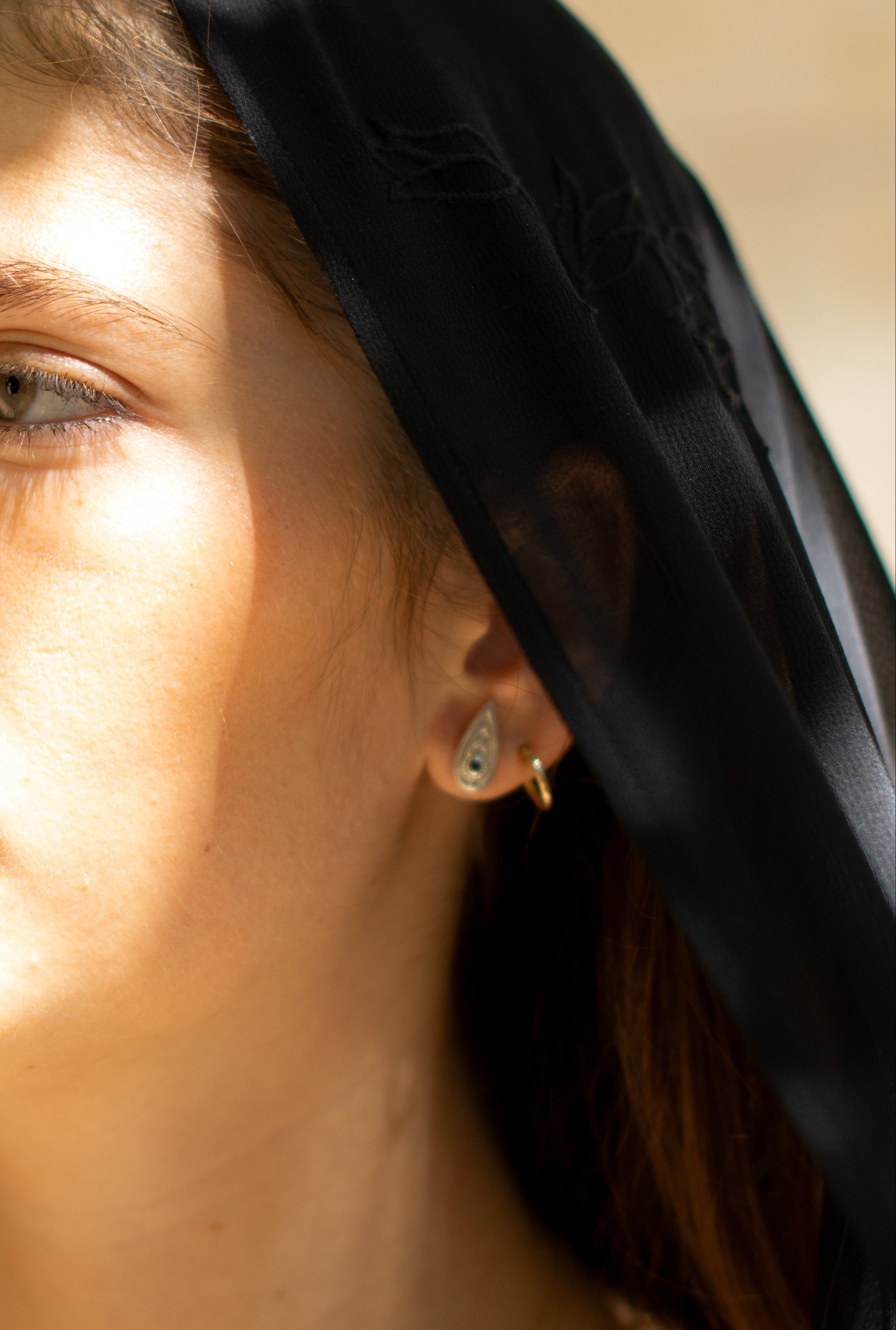side profile of a woman wearing a small teardrop-shaped silver earring set with a blue gemstone